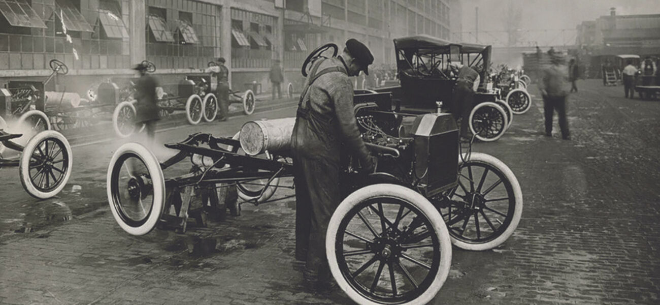 Men assembling cars on a brick-covered lot in the early 1900s