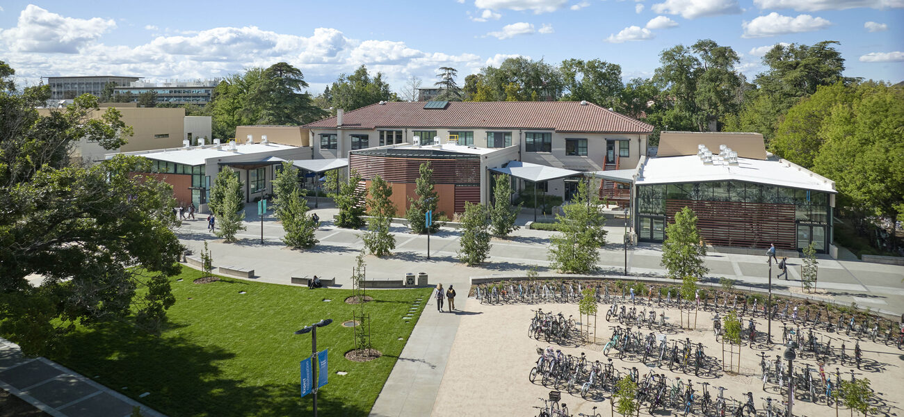 Building exterior with a plaza in front and several large bike racks full of bikes.