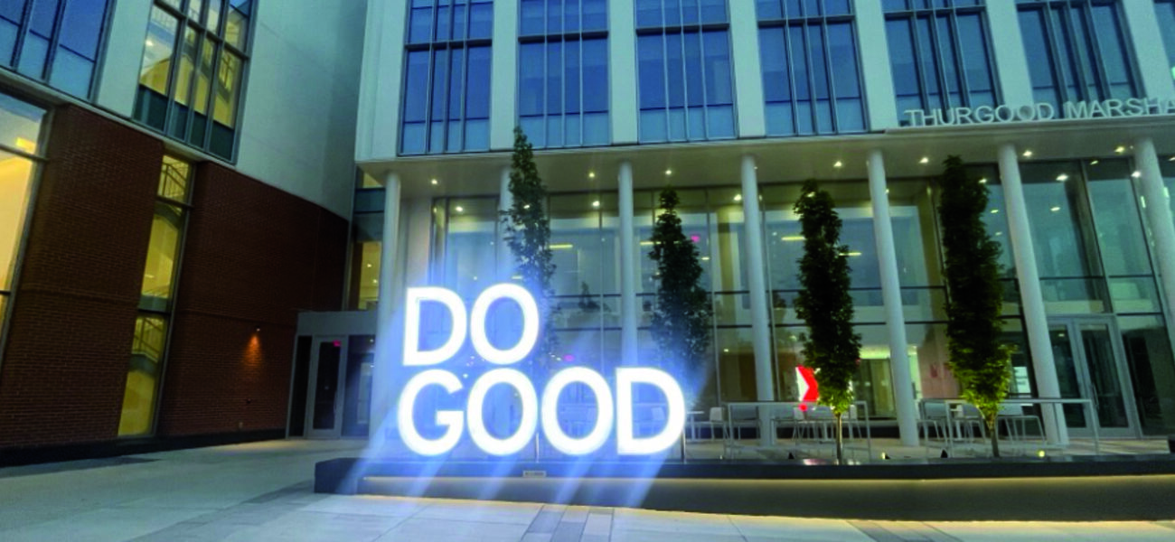 A large sign saying Do Good stands in a plaza outside a building.