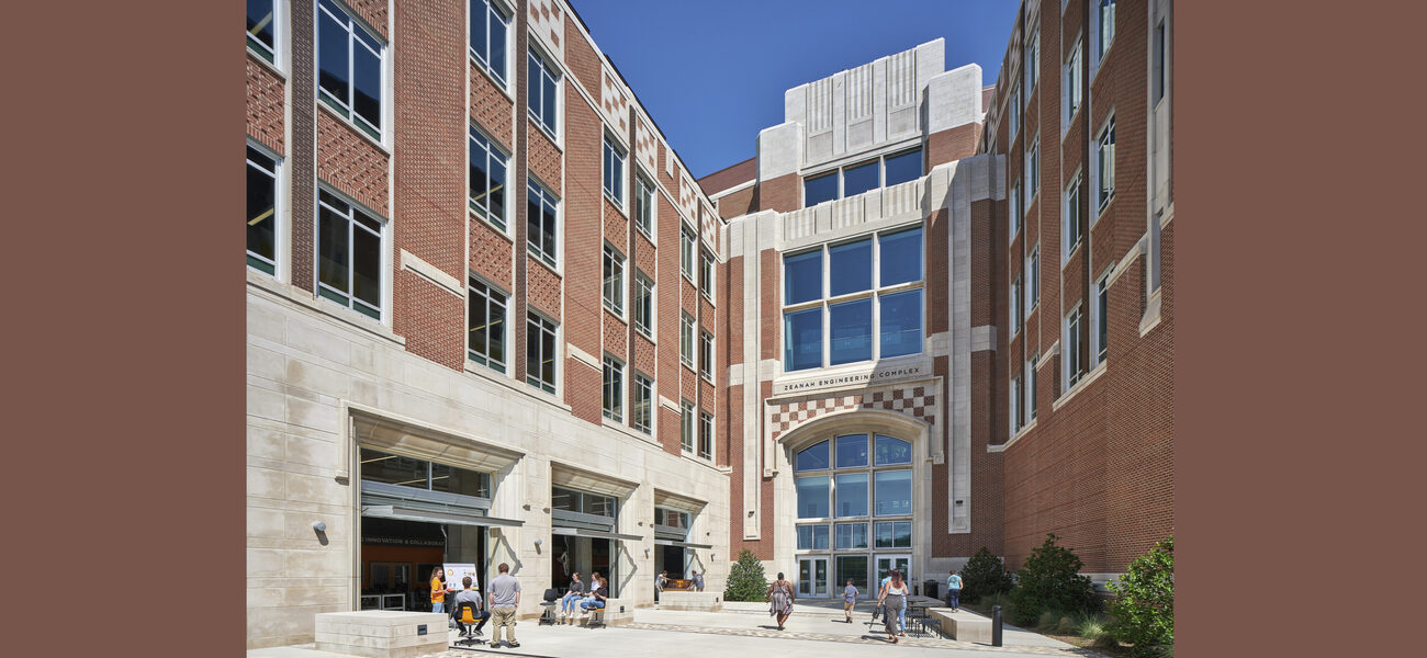 College students gather in an outdoor plaza surrounded on three sides by tall brick buildings.
