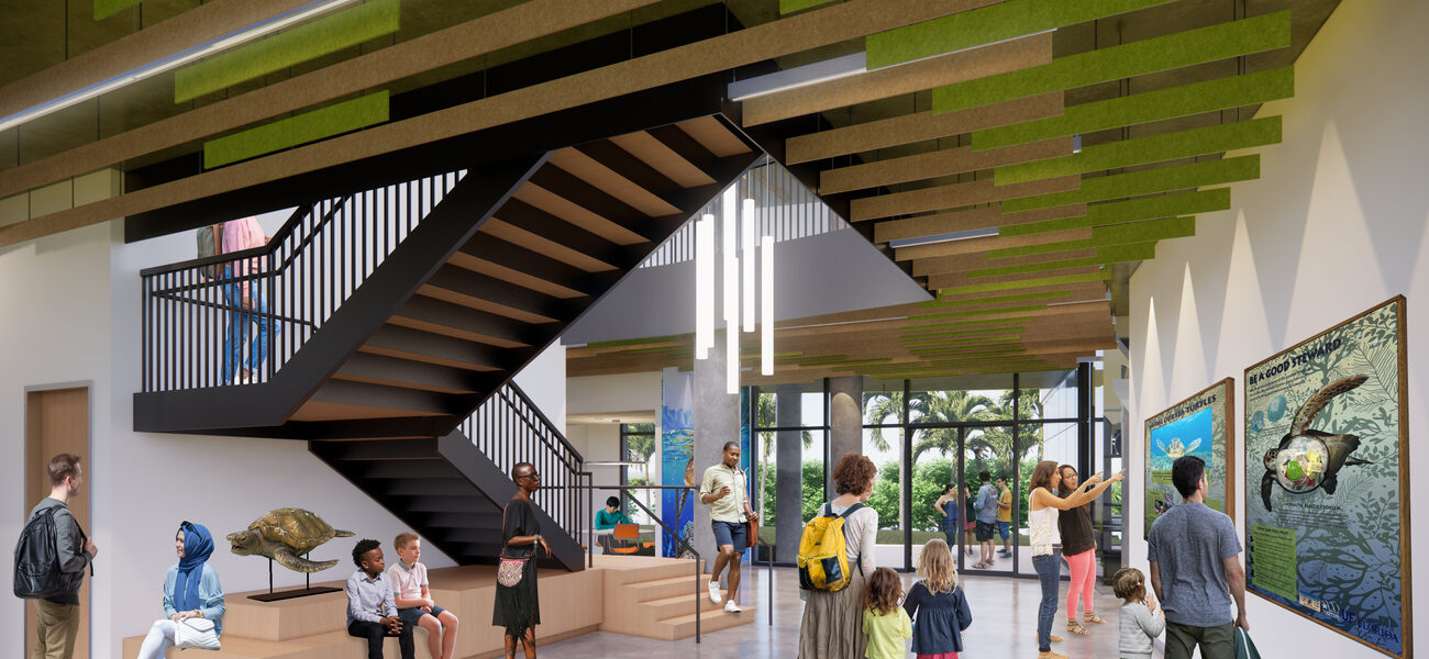 Children abnd adults mill around a large lobby with a staircase on one side and a wall covered with pictires of sea turtles