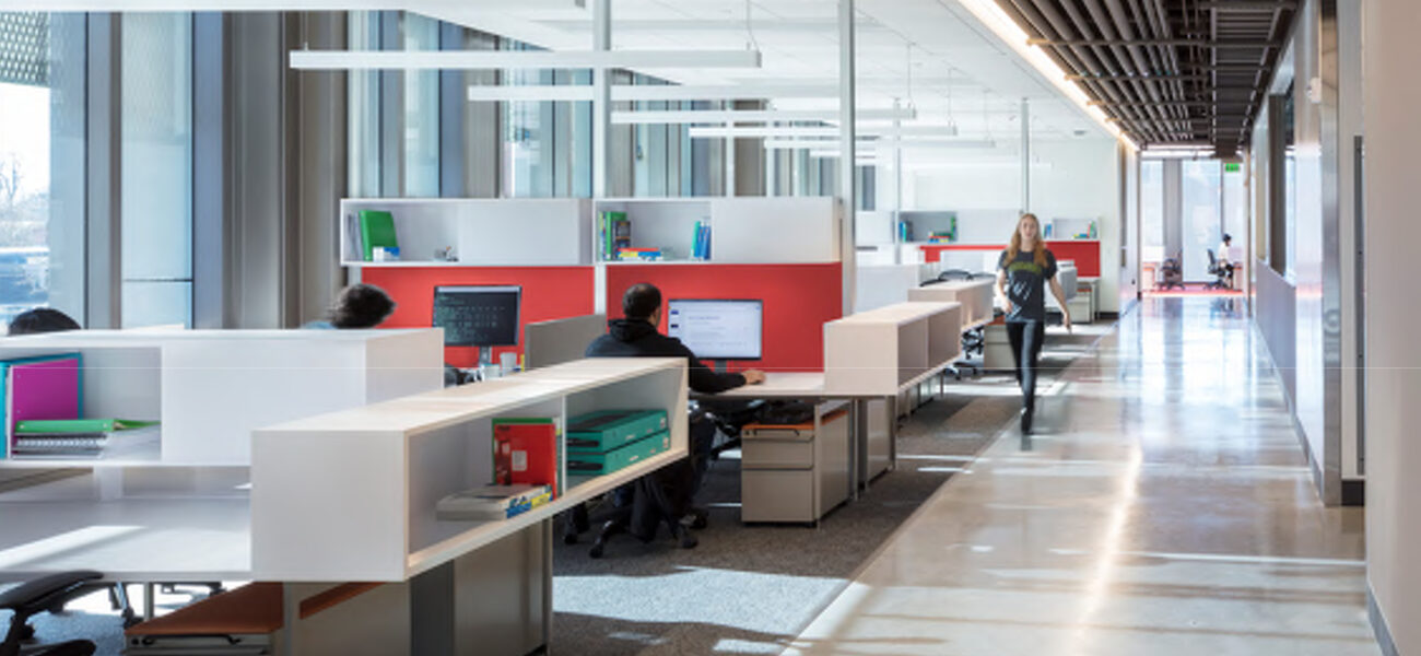 A woman walks down a hallway past people working alone at desks.