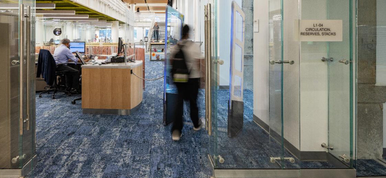 A man passes through a glass door in a glass wall into a large room