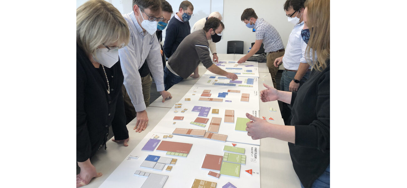 Men and women stand at a long table looking at and moving blocks representing parts of the building.