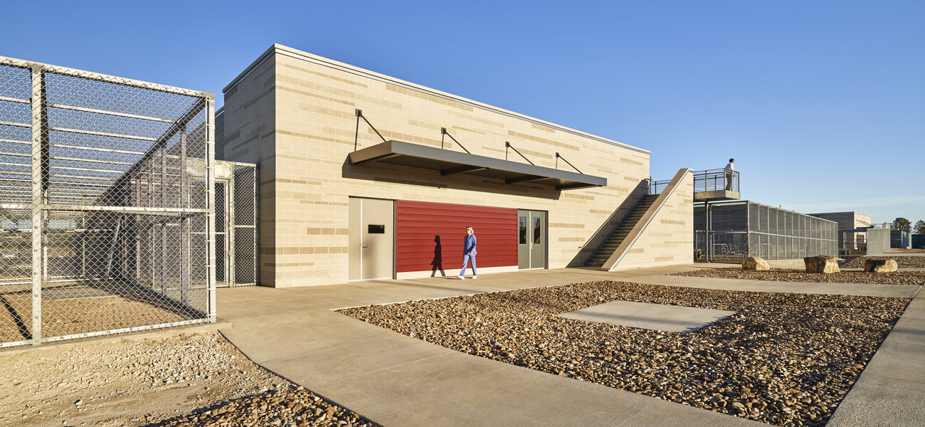 A large concerte building flanked on either side by outdoor space enclosed in chain-link fencing.