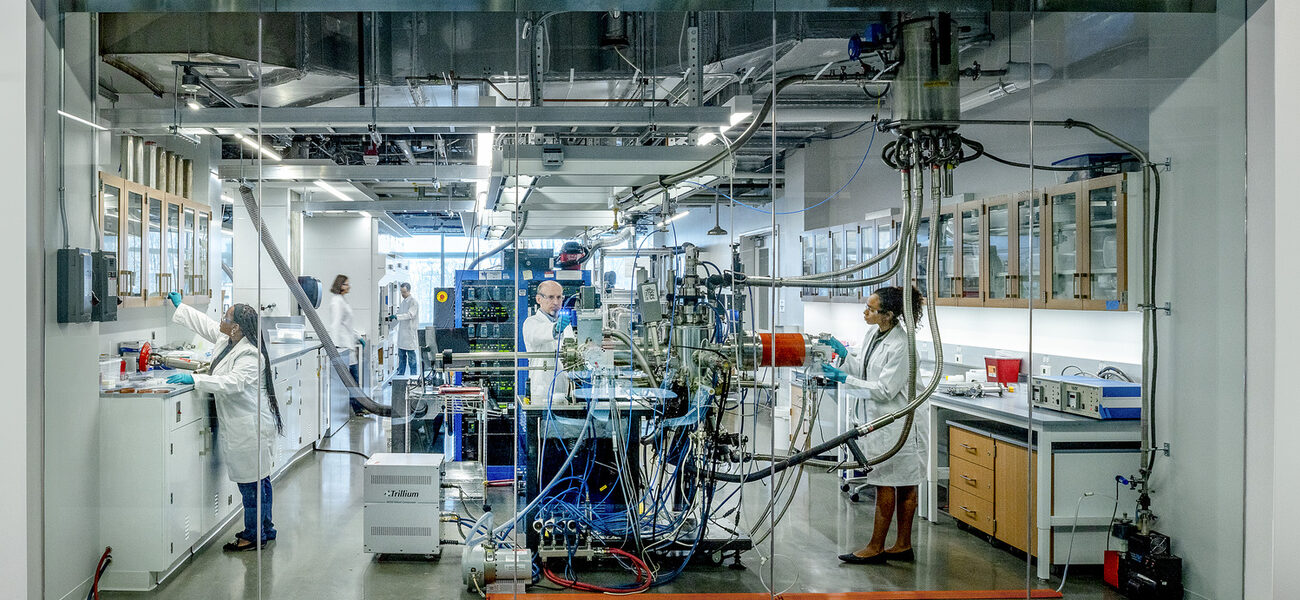 Two women and one man work on lab benches in a room full of electronic equipment.