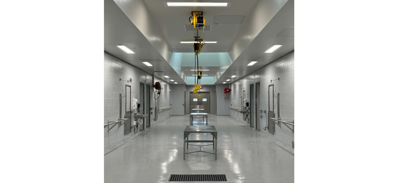 A wide hallway with stainless steel tables in hte center and closed doors on either side.