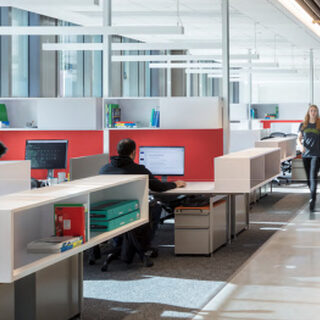 A woman walks down a hallway past people working alone at desks.