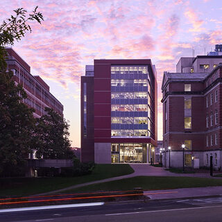 A multi-story brick building with large windows stands between two other brick buildings.