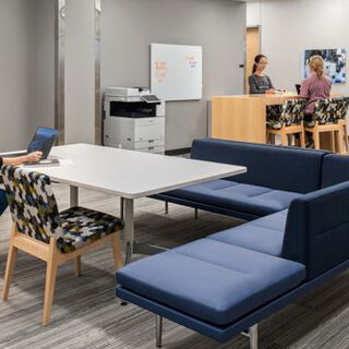 A woman sits alone at a table, working on a computer, while two other women sit together at a counter.