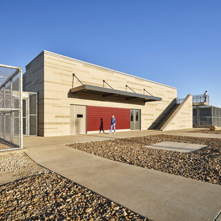 A large concerte building flanked on either side by outdoor space enclosed in chain-link fencing.